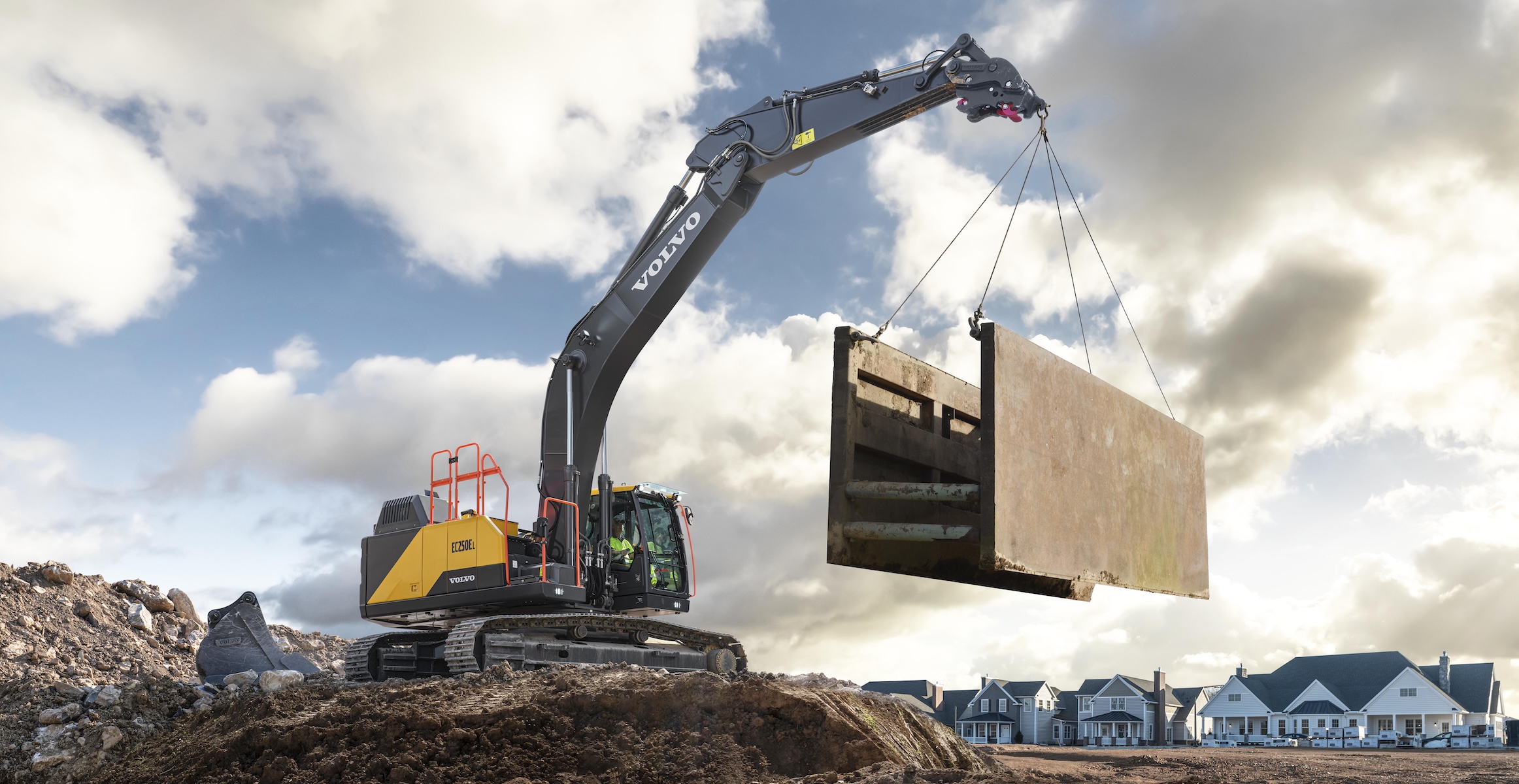 A Volvo excavator lifting a trench box at a residential building site.