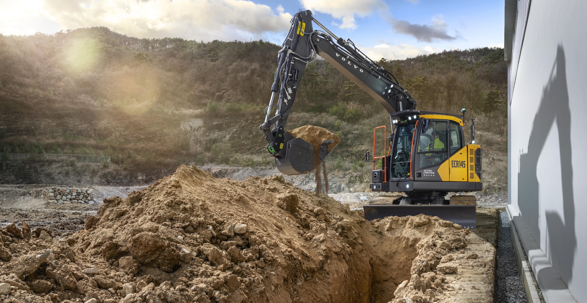 A Volvo ECR145 excavator digging a trench next to a building.