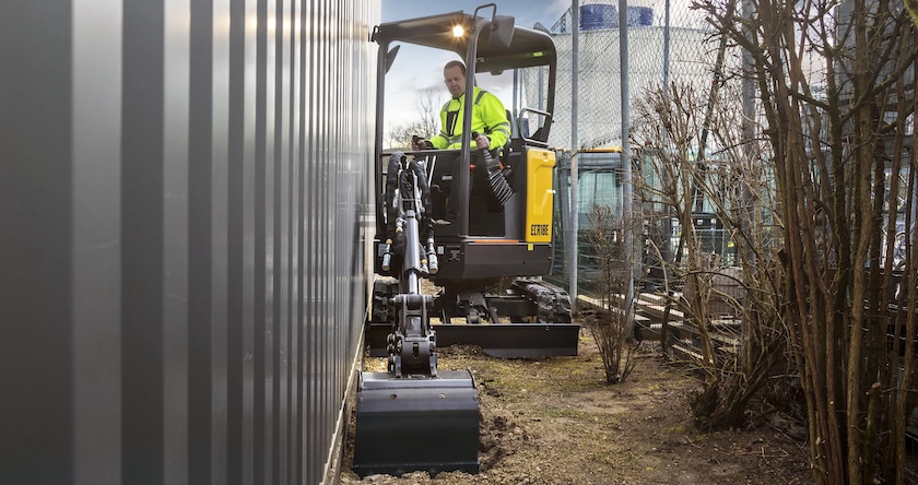 A Volvo ECR18 excavator digging a utility trench next to a building.