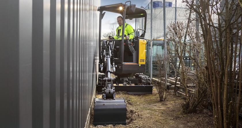 A Volvo ECR18 excavator digging a utility trench next to a building.