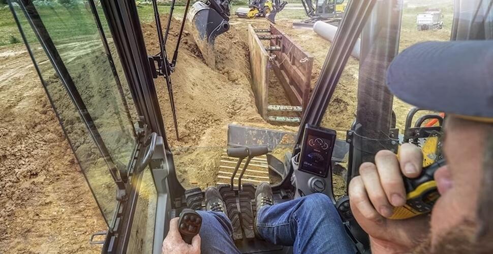 An operator in a Volvo excavator communicating with other crewmembers while trenching on a construction jobsite.