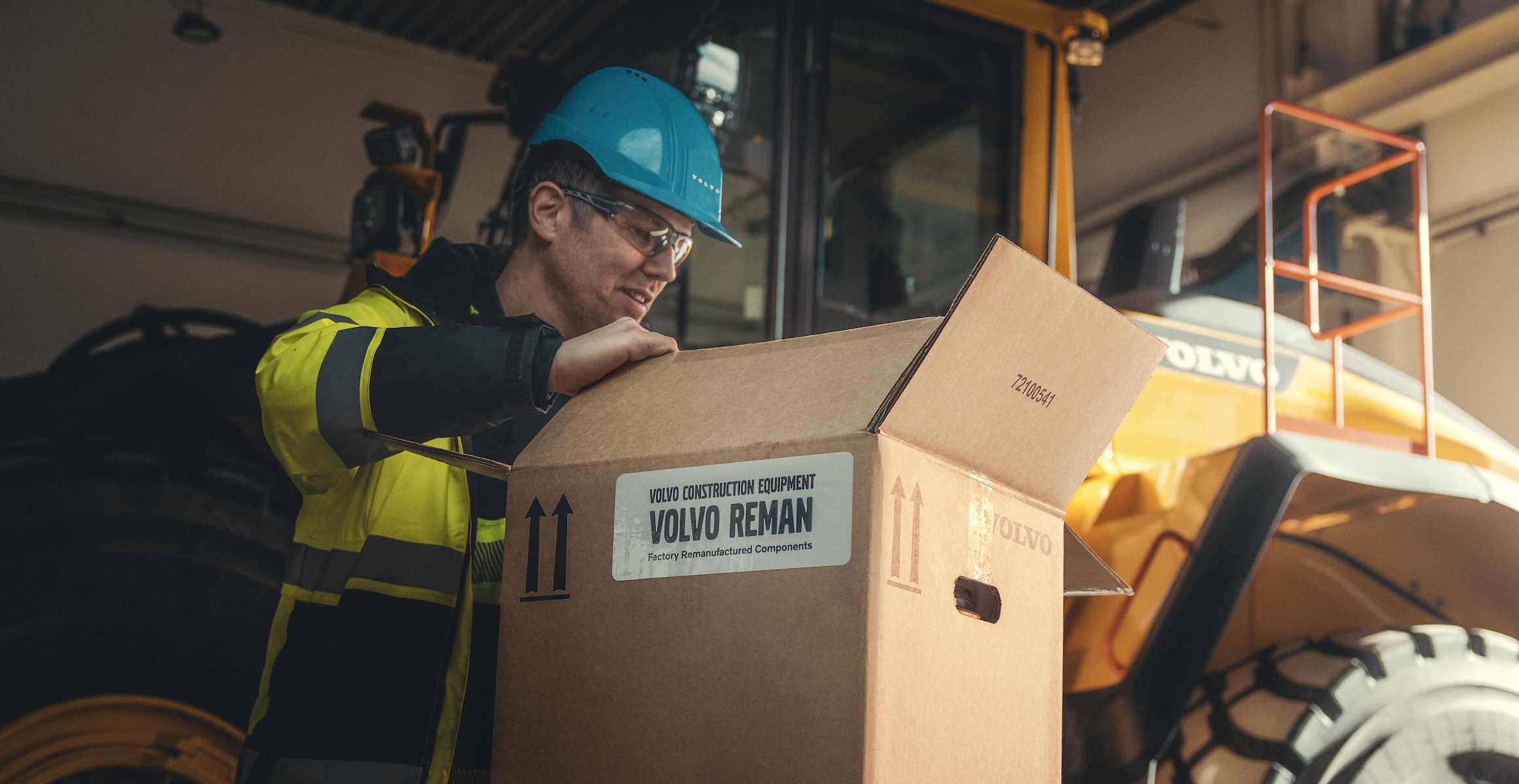 A service tech in front of a Volvo wheel loader opening a box with Volvo Reman parts in it.