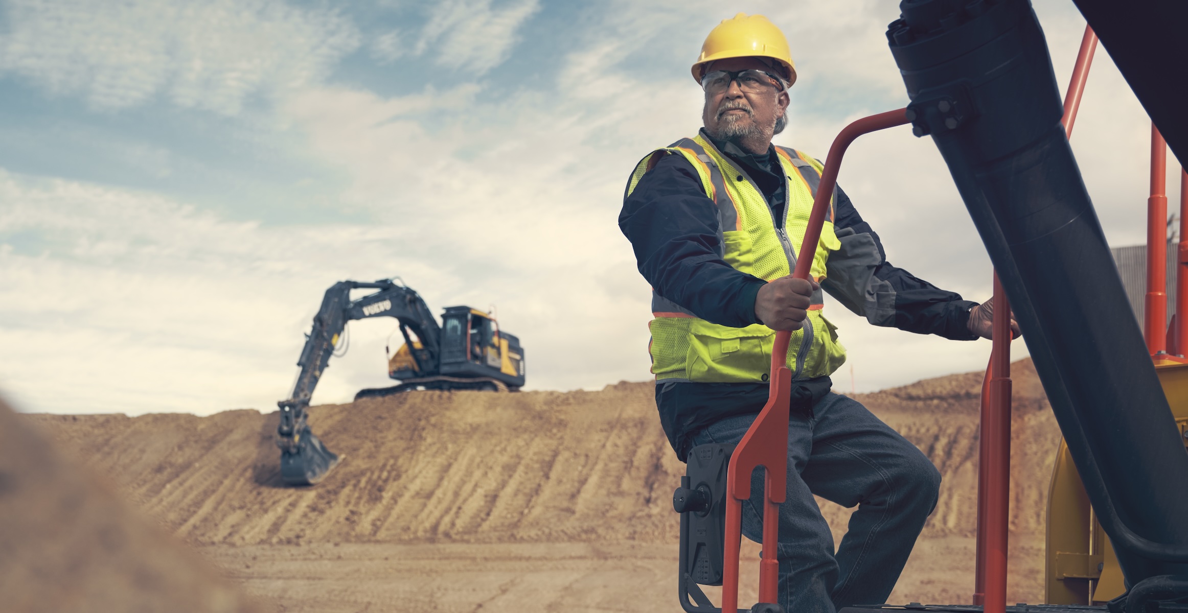 An operator from a tier-2 subcontractor climbing into a Volvo ADT in the foreground with a Volvo excavator moving dirt in the background. 