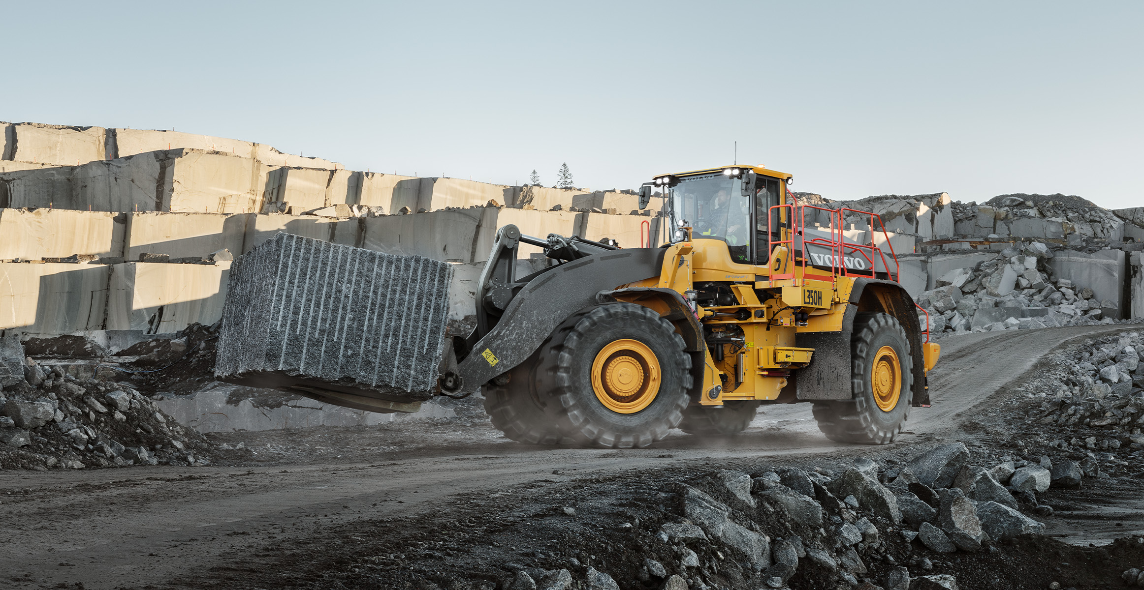 A Volvo L350H wheel loader carrying a block of rock in a quarry.