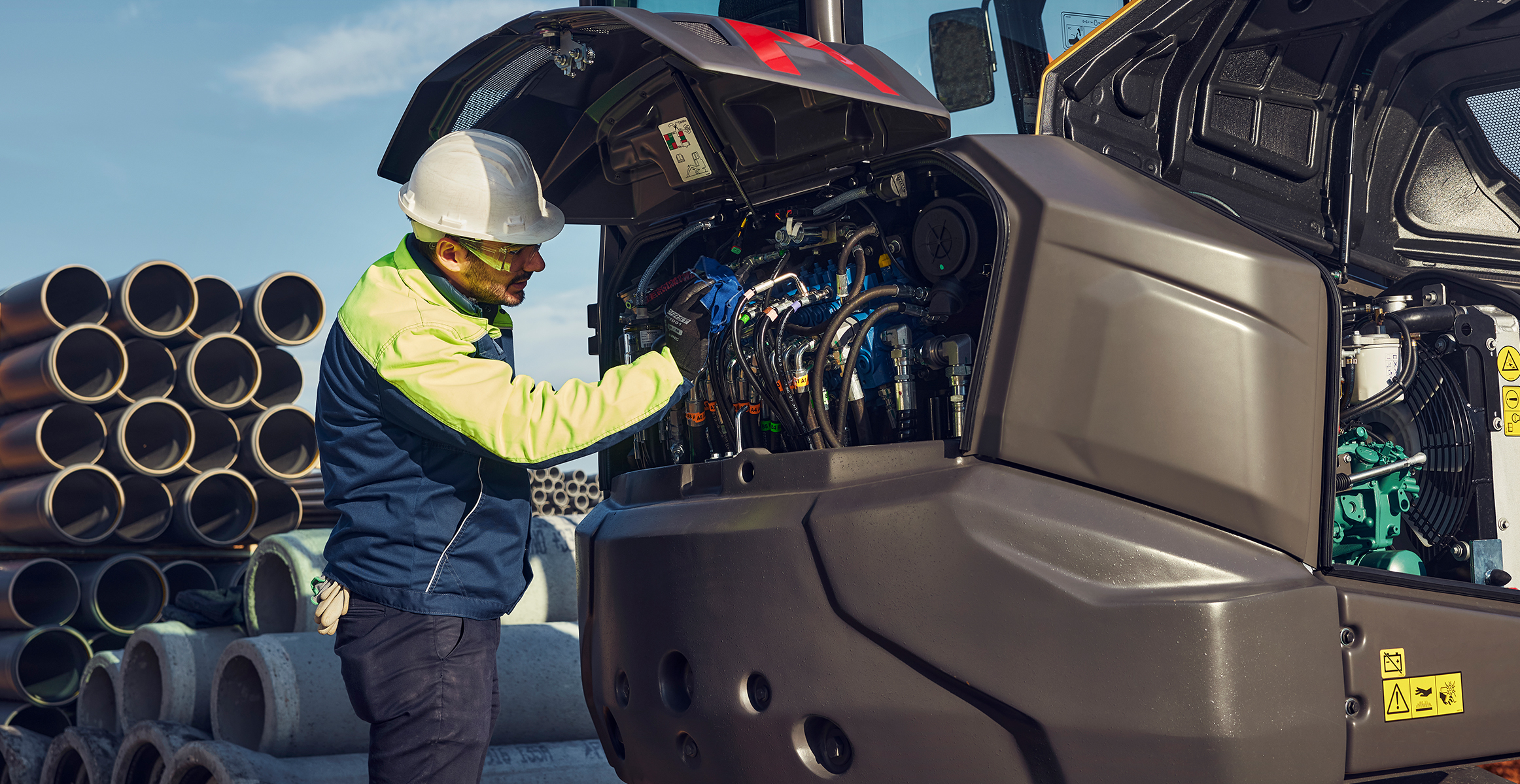A service tech working on a piece of heavy construction equipment with the service compartment open.