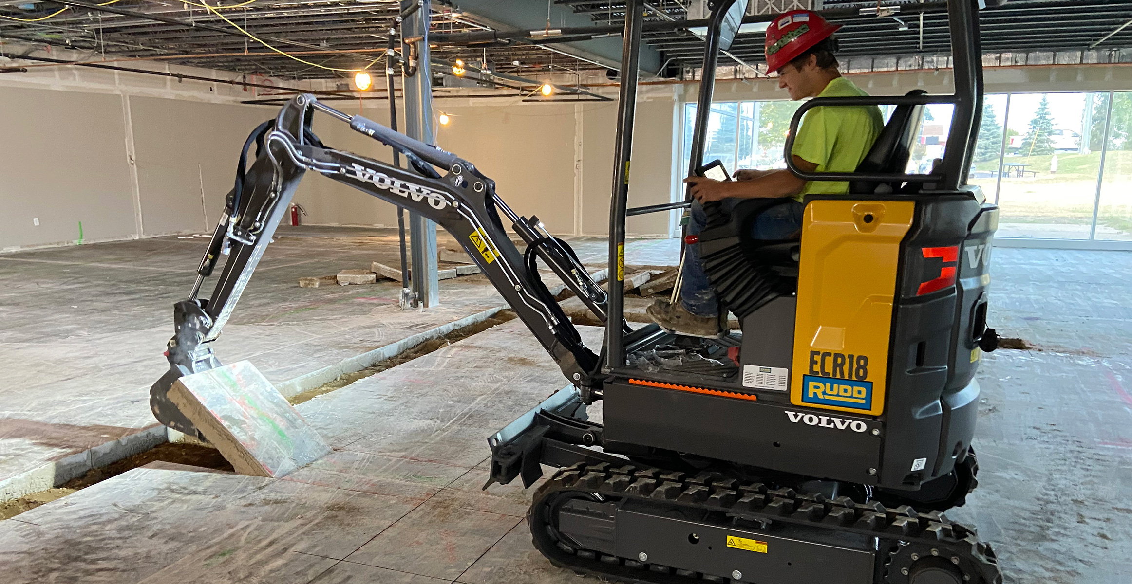 A Volvo ECR18 Electric compact excavator lifts concrete slabs on an indoor jobsite.