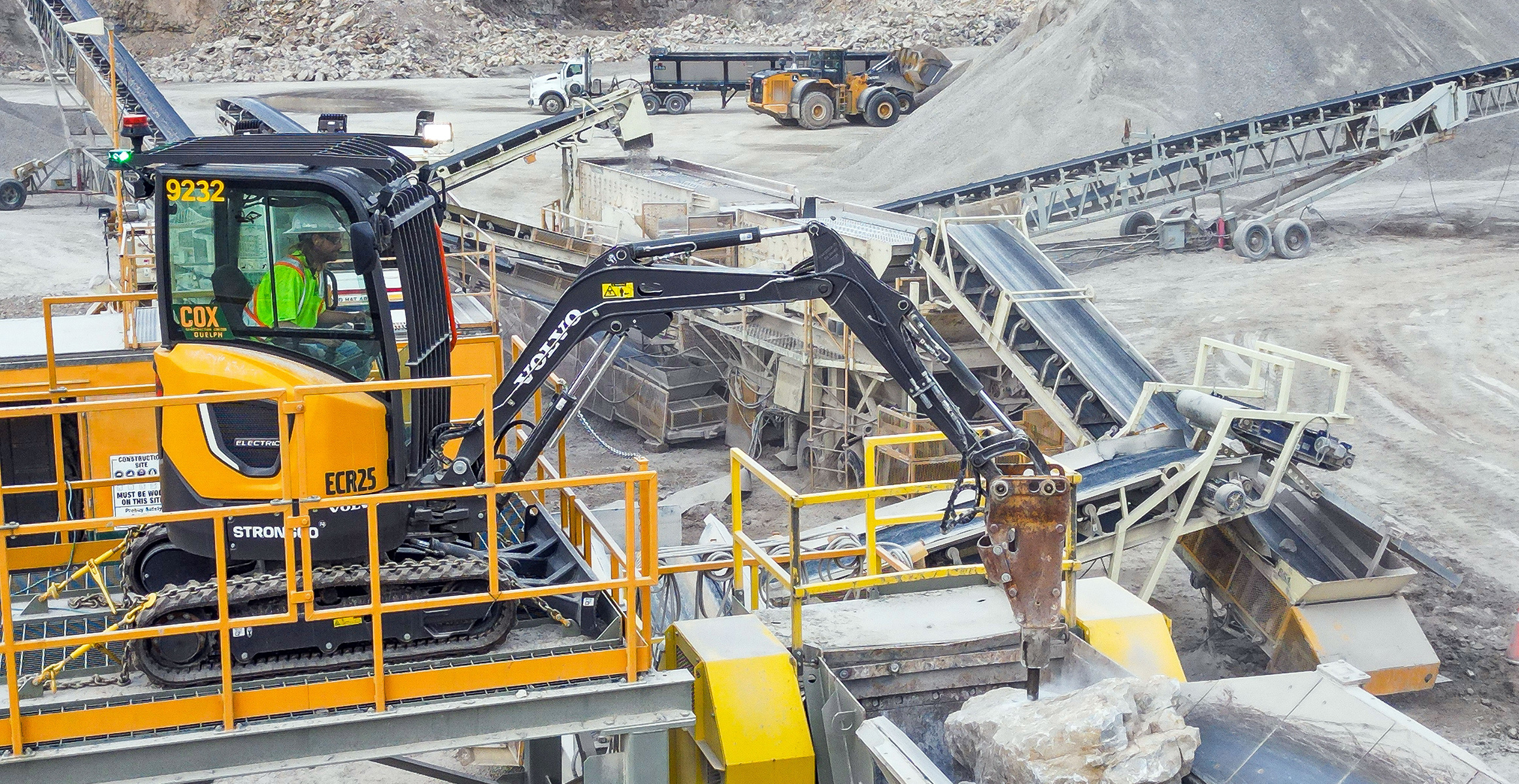 Cox Construction uses a Volvo ECR25 Electric compact excavator to break large rocks atop a large crusher at a quarry site.
