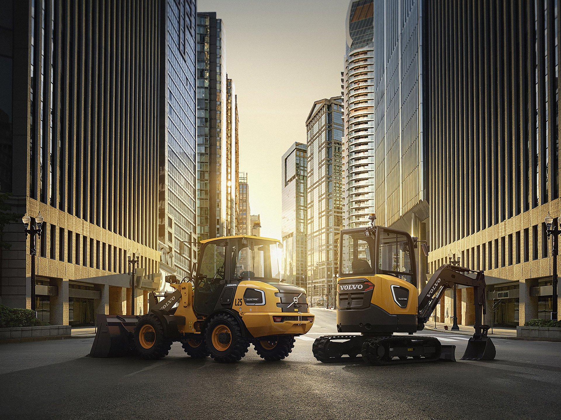 A Volvo L25 Electric and a Volvo ECR25 Electric on an empty city street with the sun setting behind on the horizon.