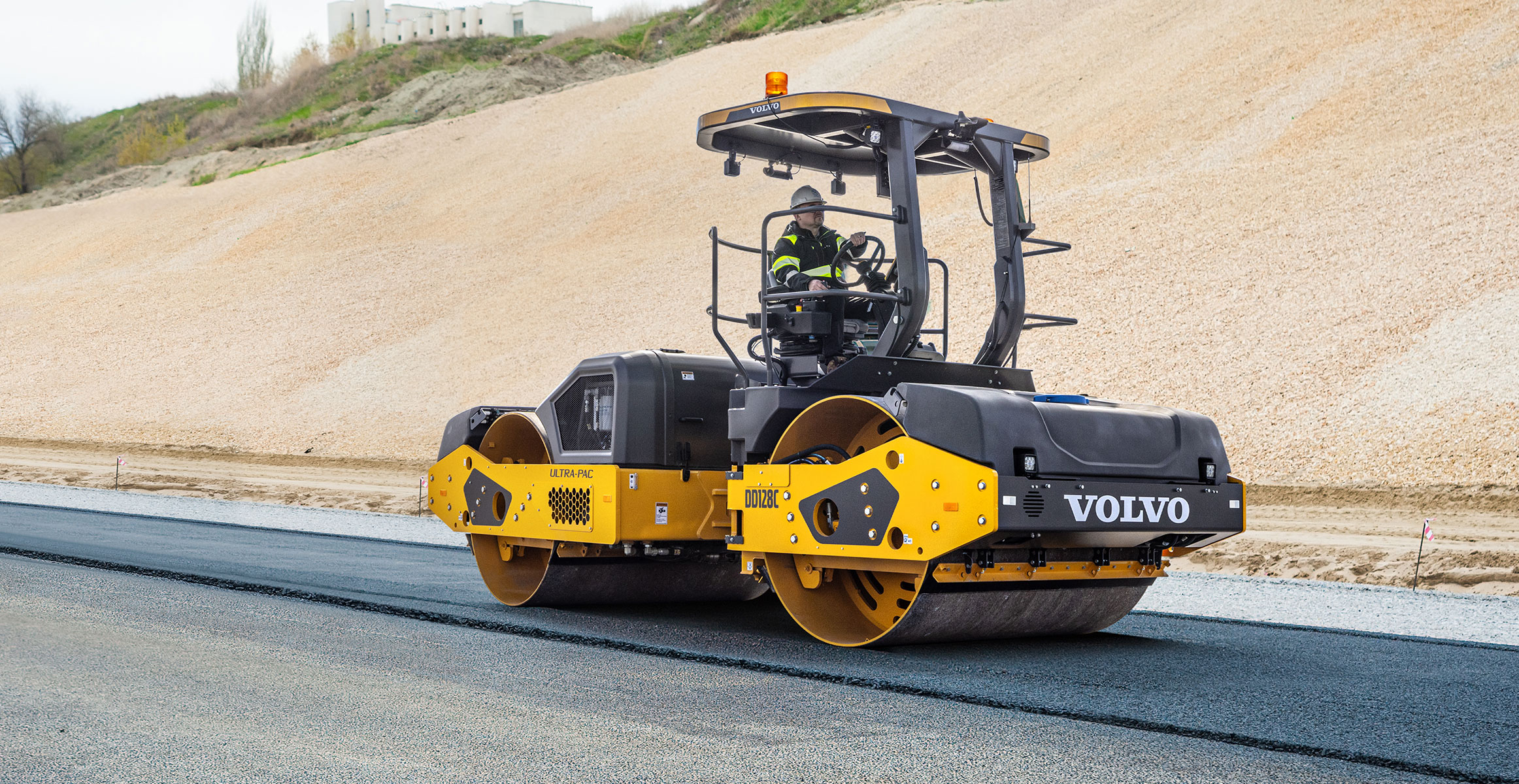 A Volvo asphalt compactor rolling the surface course of a new road.