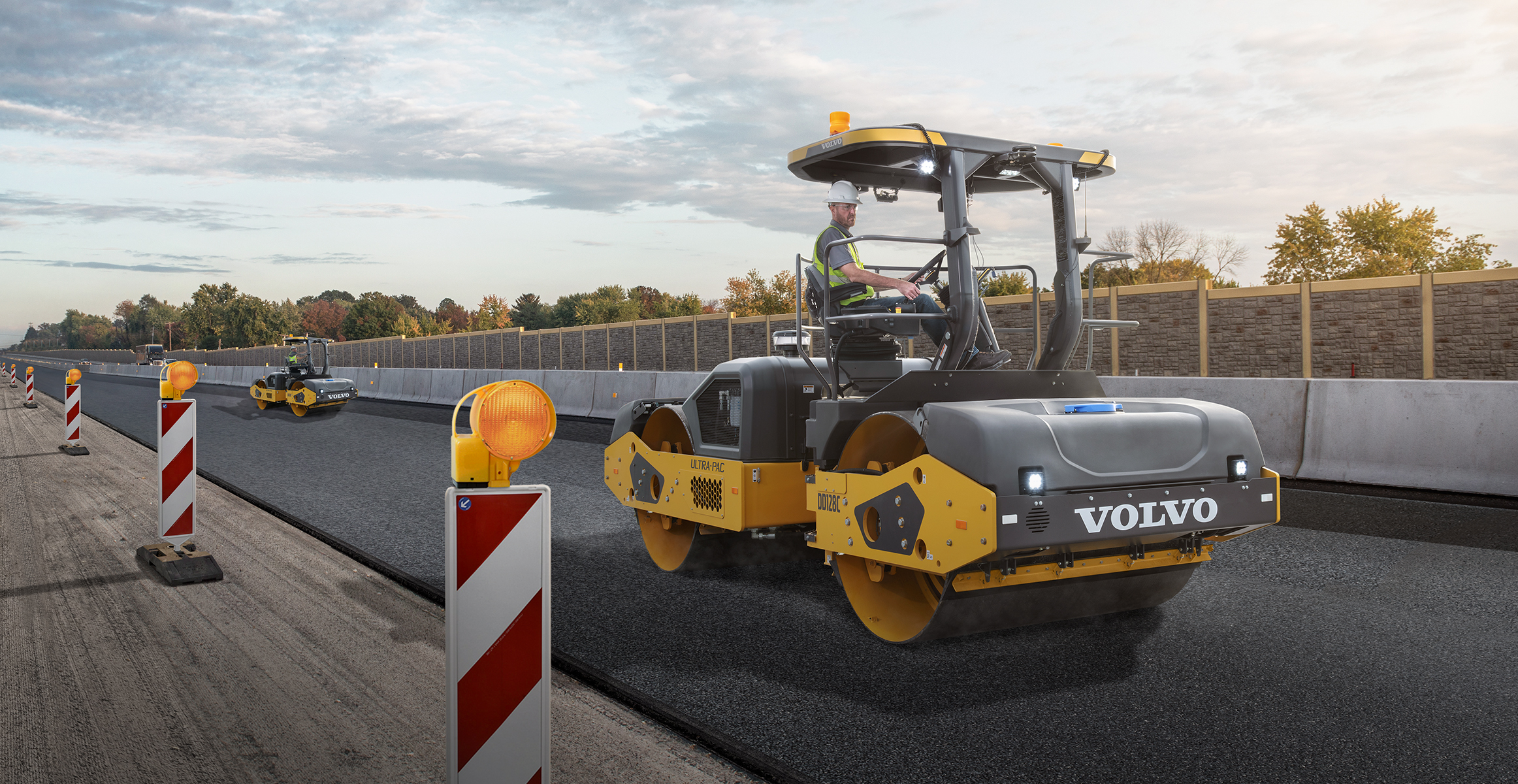 Two Volvo construction compactors rolling out an asphalt mat of a new highway.