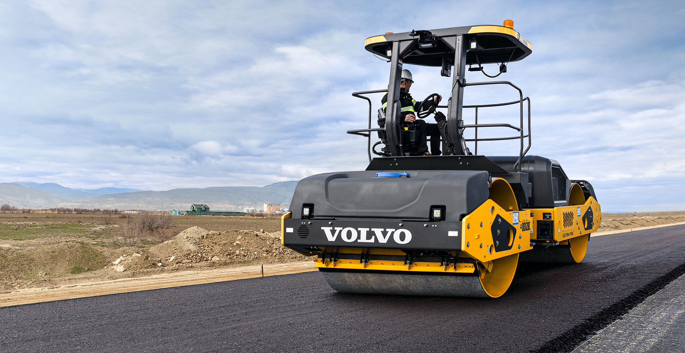 A Volvo asphalt compactor rolling the mat of a new road.