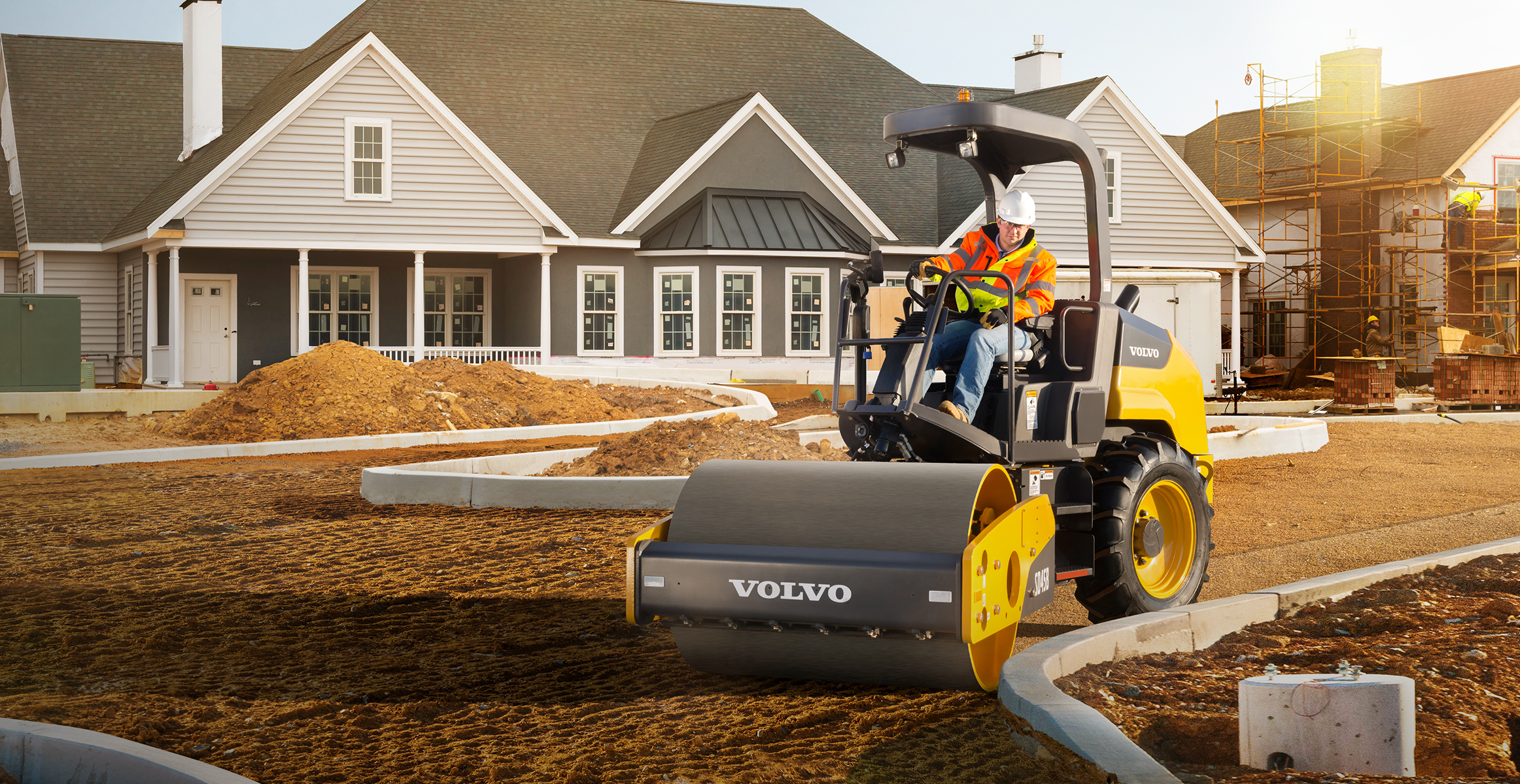 A Volvo dirt roller prepping the subbase of a new driveway in residential construction.