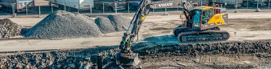 A Volvo EC230 Electric midsize excavator digging a foundation on a construction site.