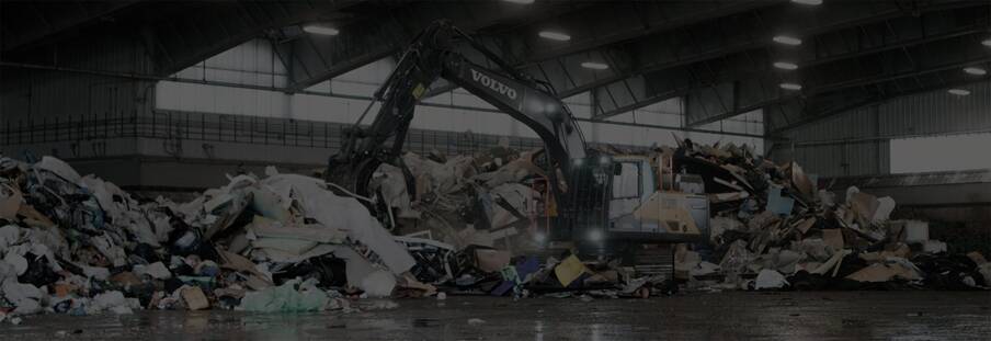 A black and white image of a Volvo EC230 Electric excavator processing waste at a transfer facility.
