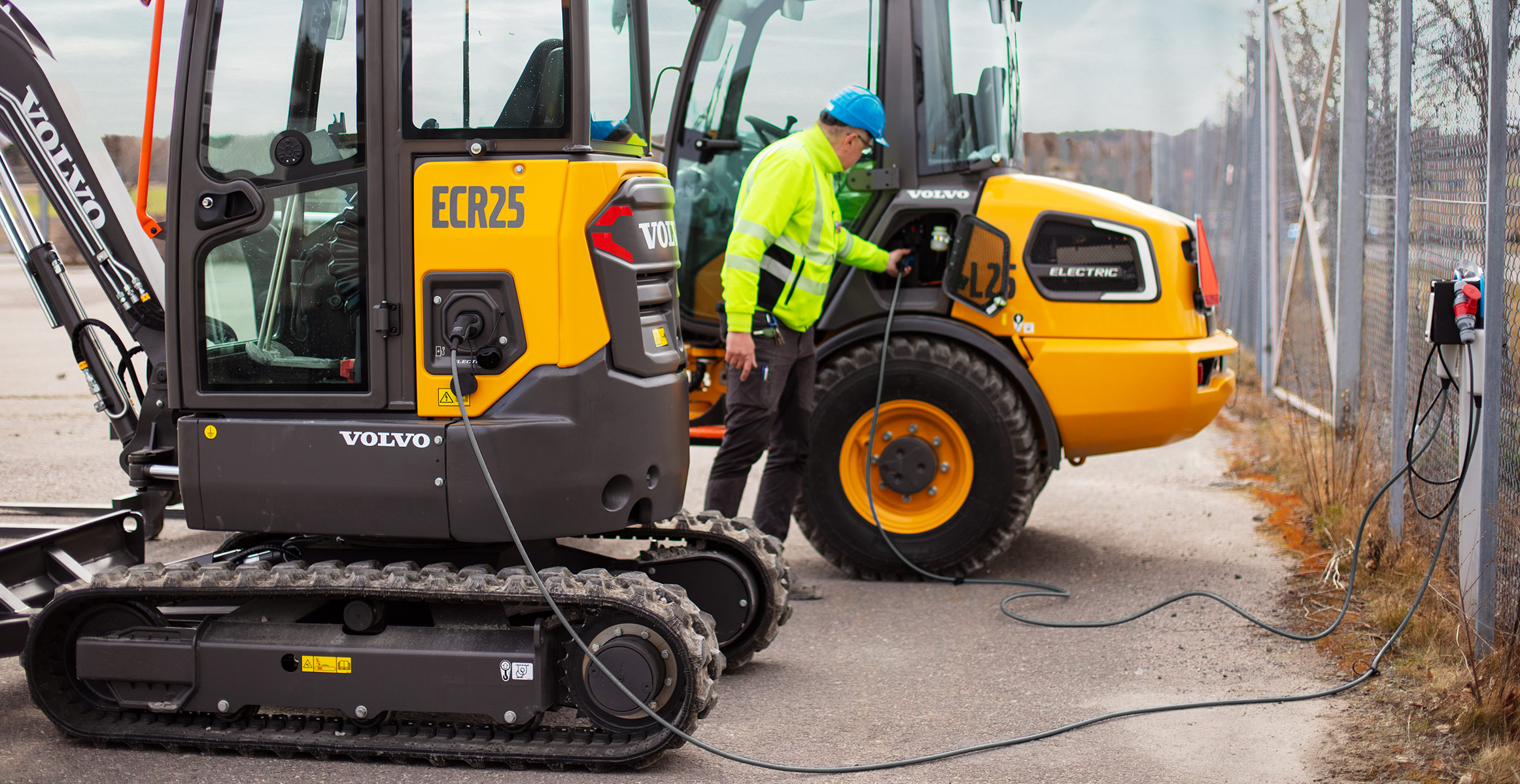 An operator charging a Volvo electric excavator and electric wheel loader.