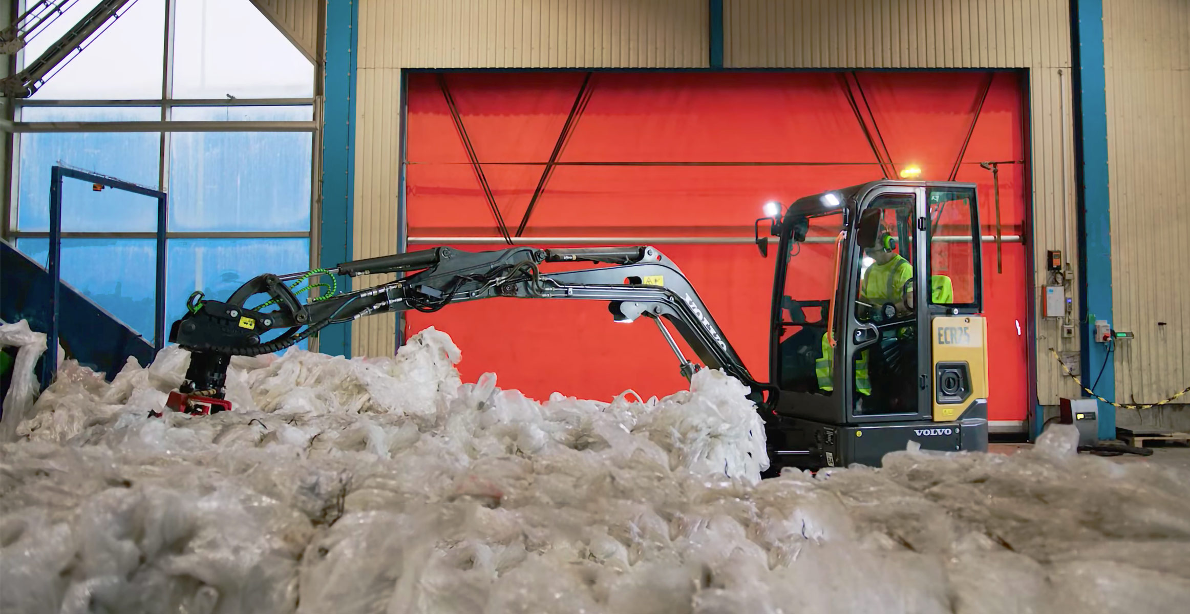 An electric excavator operator at Stena Recycling stacking bundles of recycled plastic. 