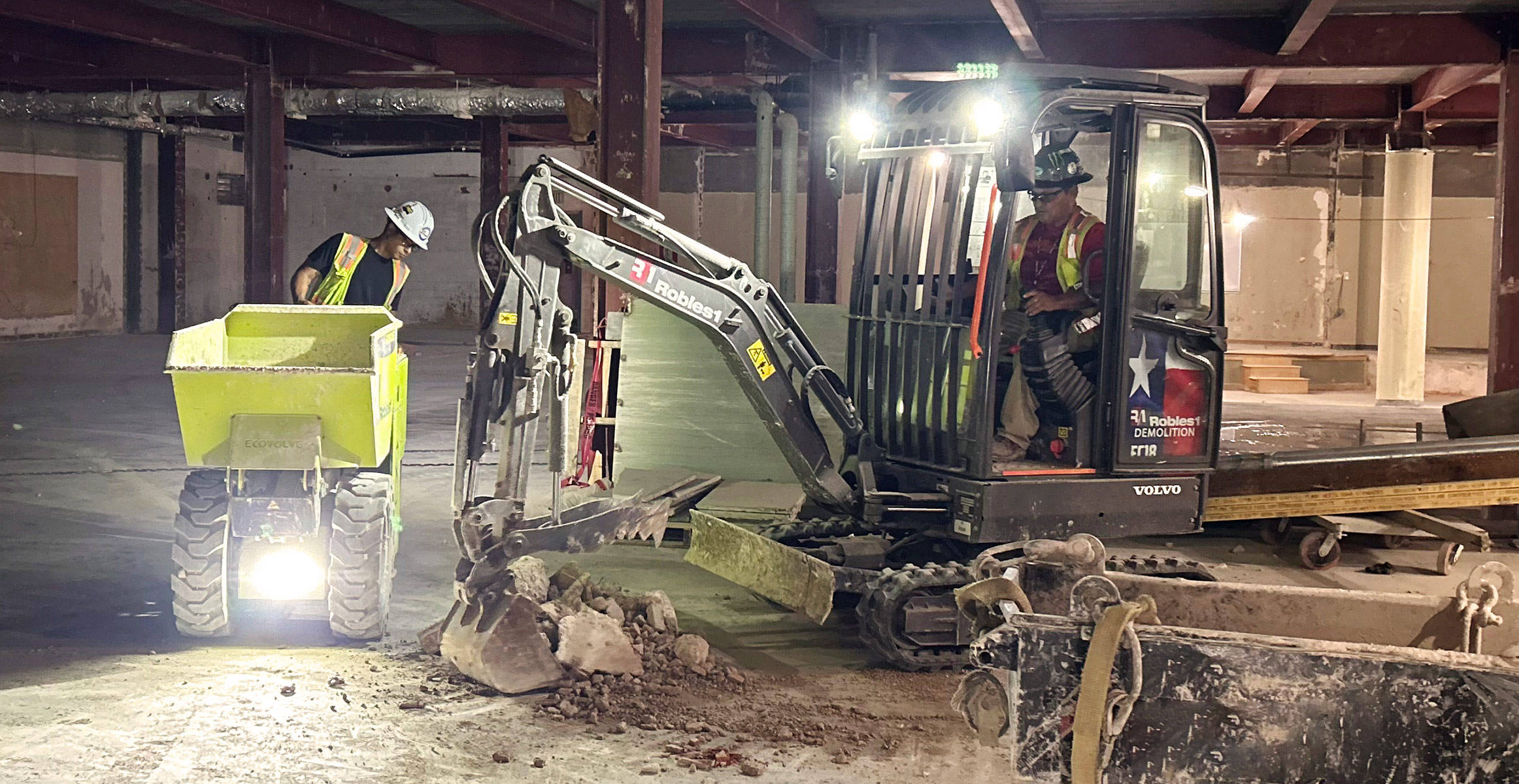 A Volvo compact electric excavator using lights to work in indoor demolition.