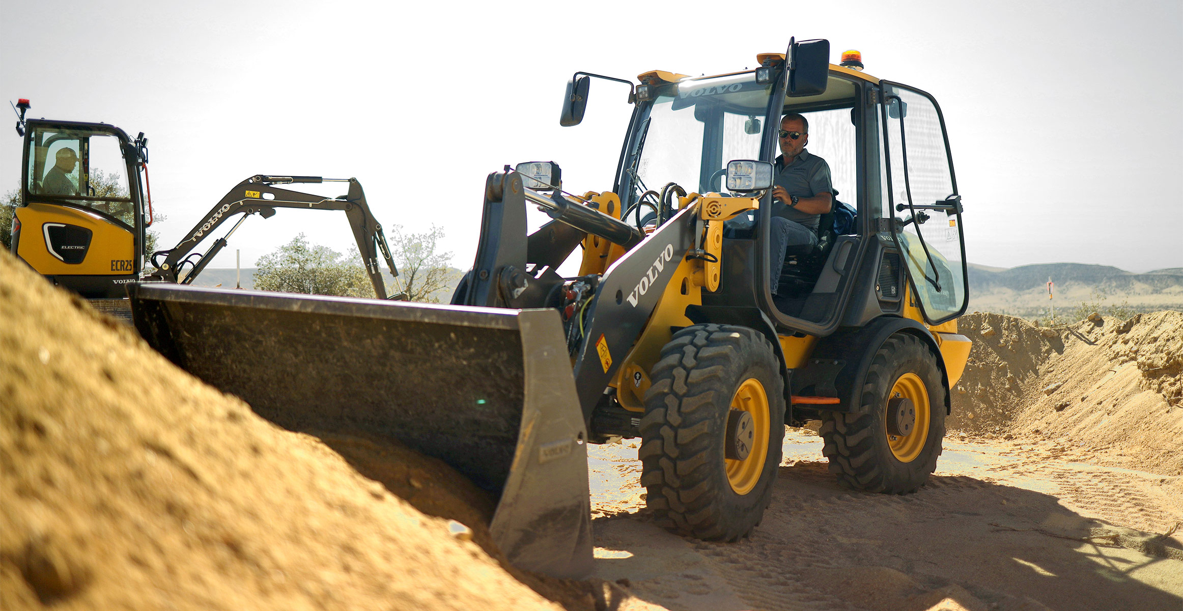A Volvo electric wheel loader loading dirt in front of a Volvo electric excavator.