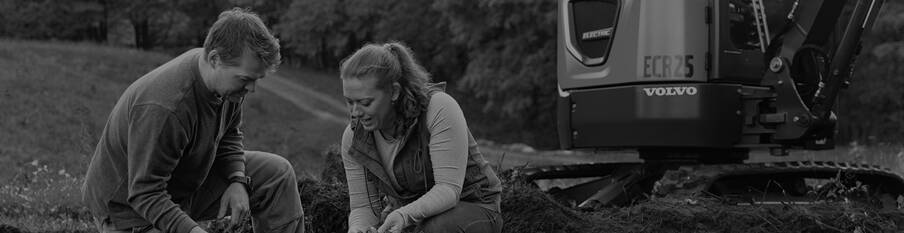 A man and a woman who own a farm crouch in front of their Volvo electric excavator.