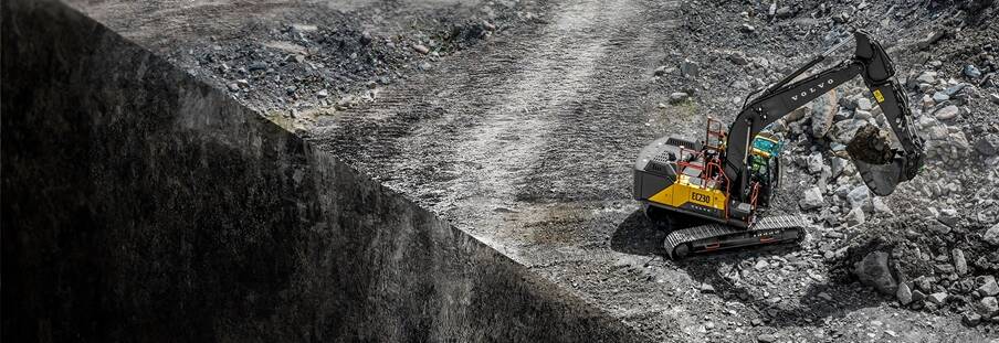 A Volvo excavator working next to the edge of a quarry that drops off vertically.