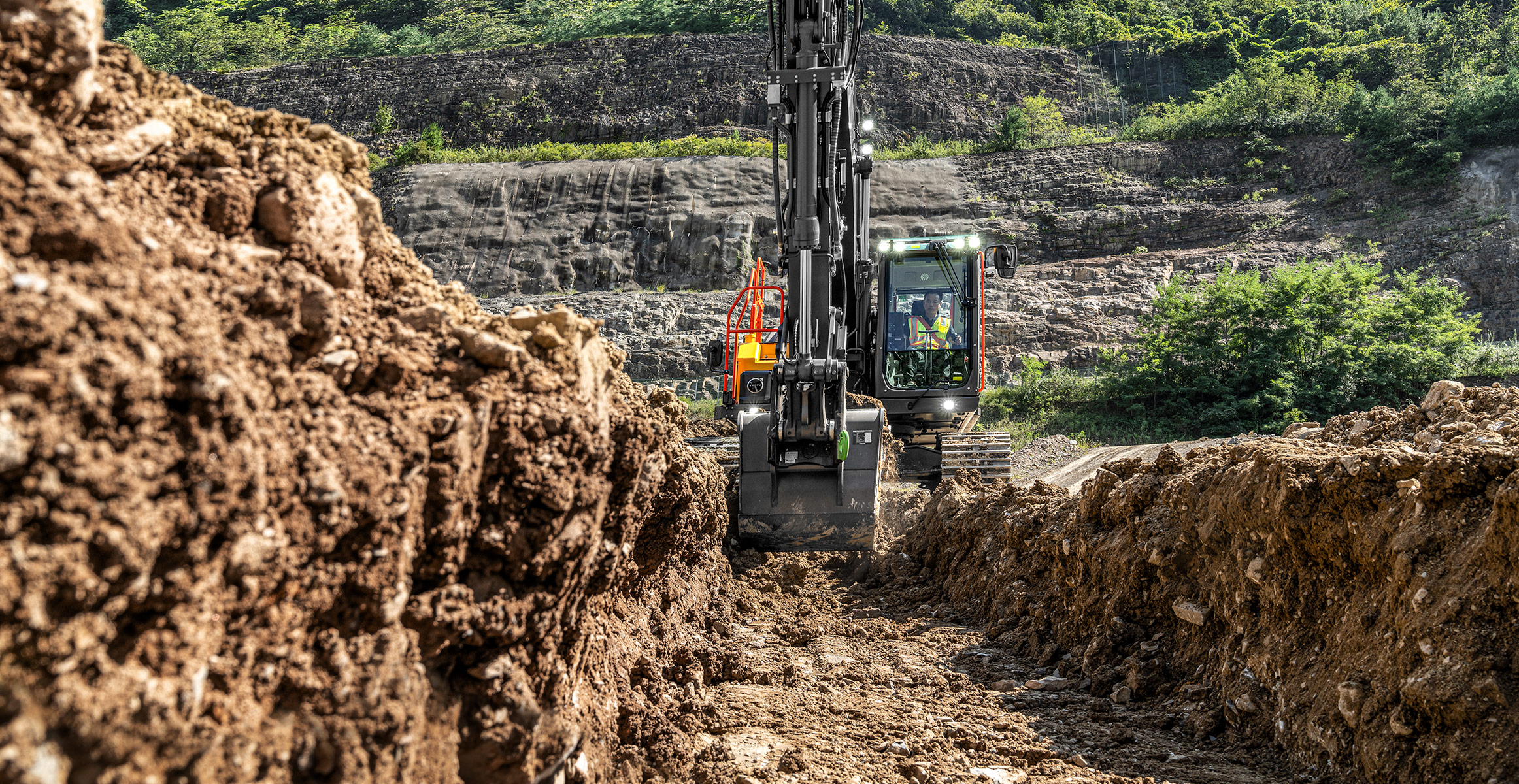 A Volvo excavator digging a trench away from the camera.