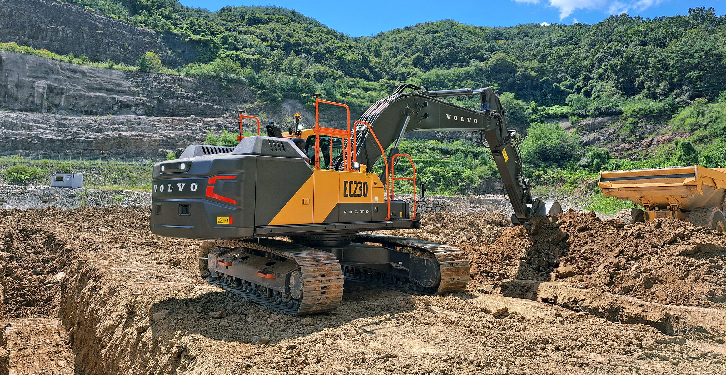 A Volvo EC230 excavator loading dirt into a Volvo articulated hauler.