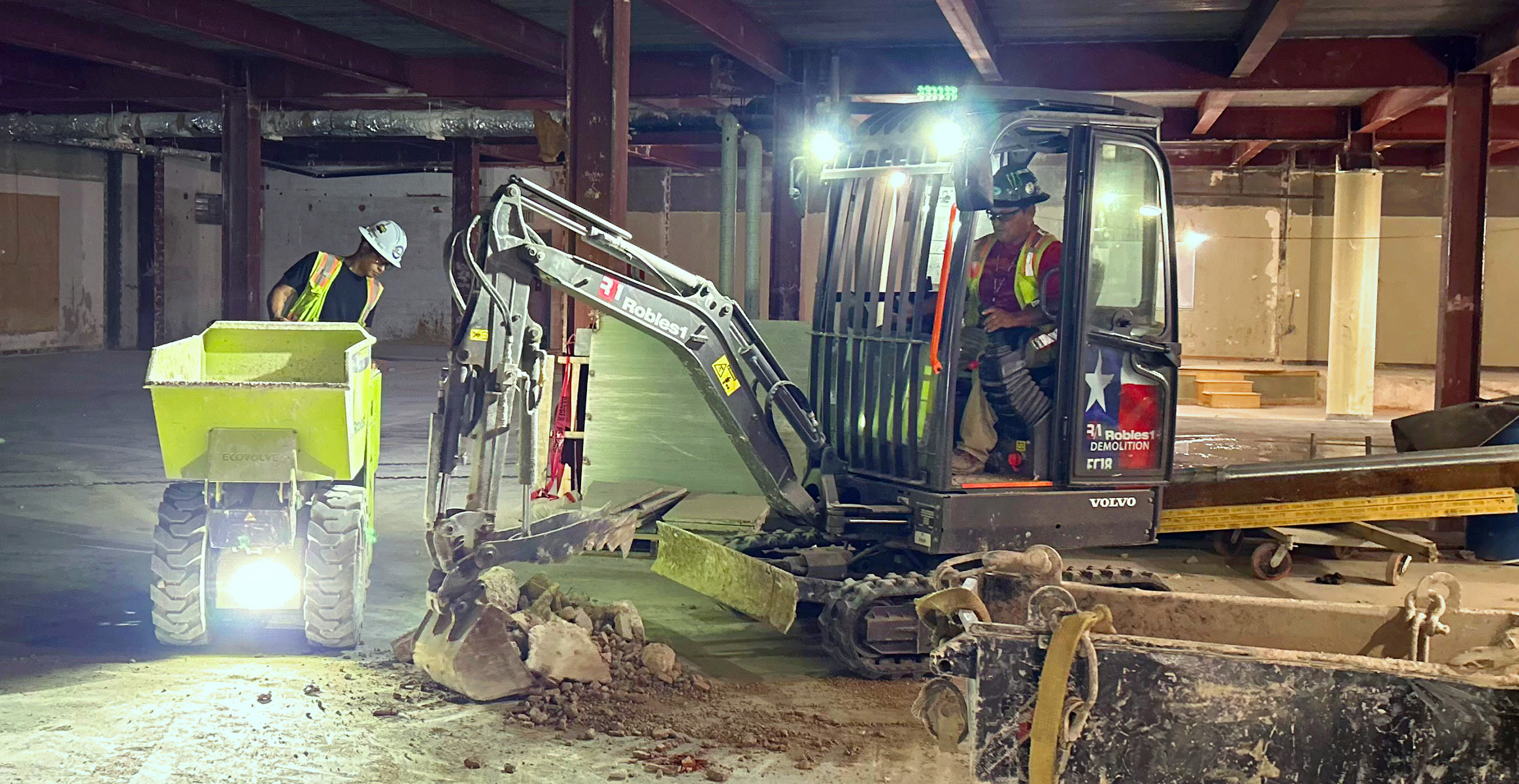 An operator using a Volvo ECR25 Electric excavator for indoor demolition next to his coworker.