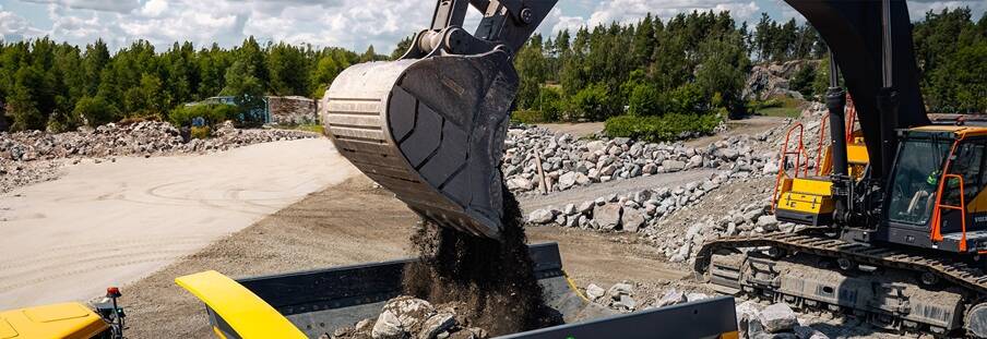 ​Close-up of a Volvo excavator dumping rock and dirt into a Volvo articulated dump truck.​ 