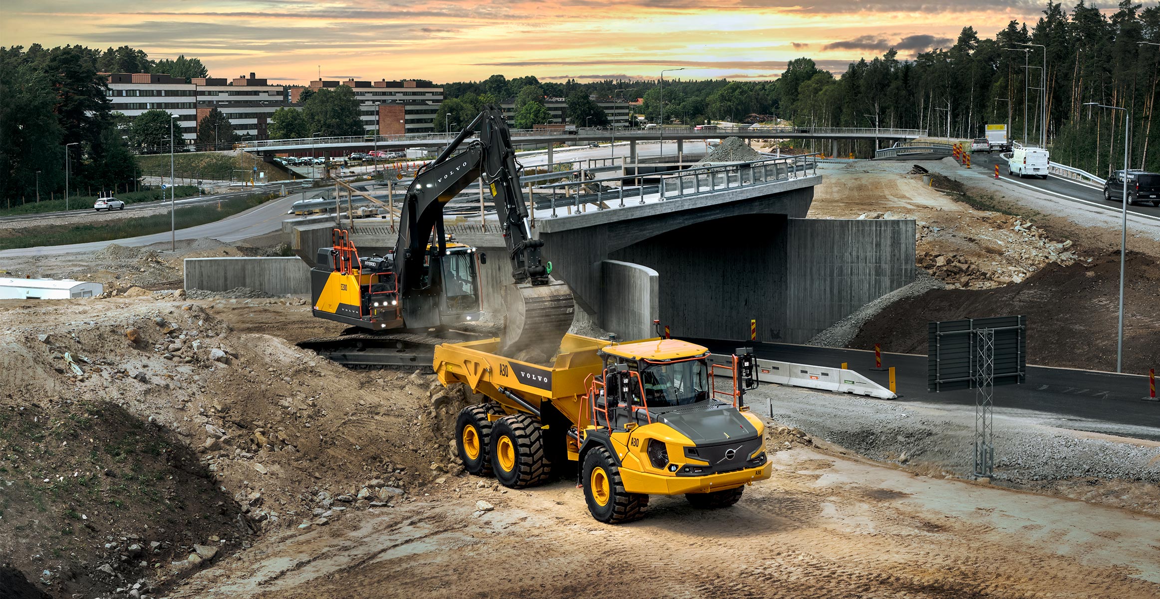 A Volvo crawler excavator loading a Volvo ADT during construction of a highway overpass.