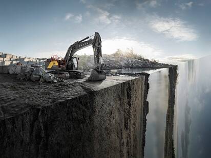 A Volvo excavator at the edge of a jobsite with a diagonal portion of the site dropping off vertically.