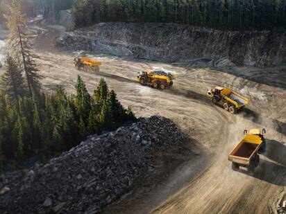 Four Volvo articulated dump trucks driving in line through a quarry.