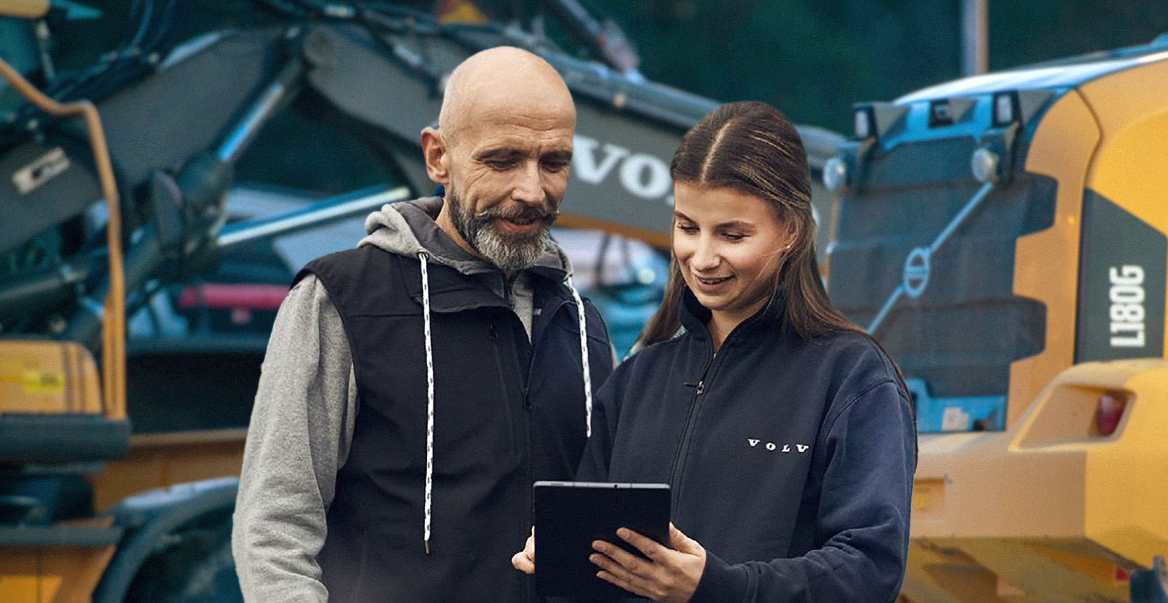A Volvo Financial Services rep working with a customer on heavy equipment financing in front of Volvo construction equipment.
