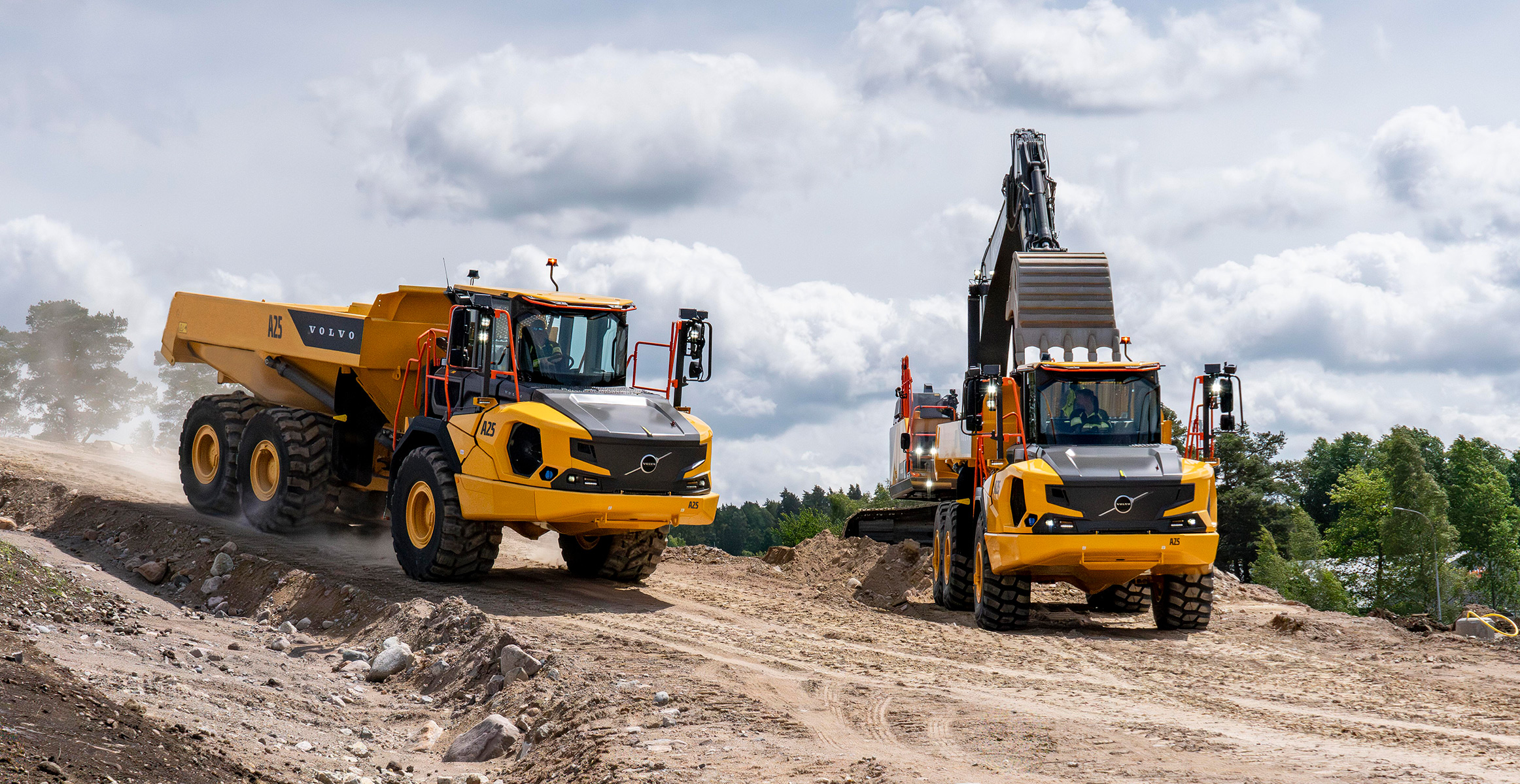 Two Volvo articulated dump trucks being loaded by a Volvo excavator on a construction jobsite.