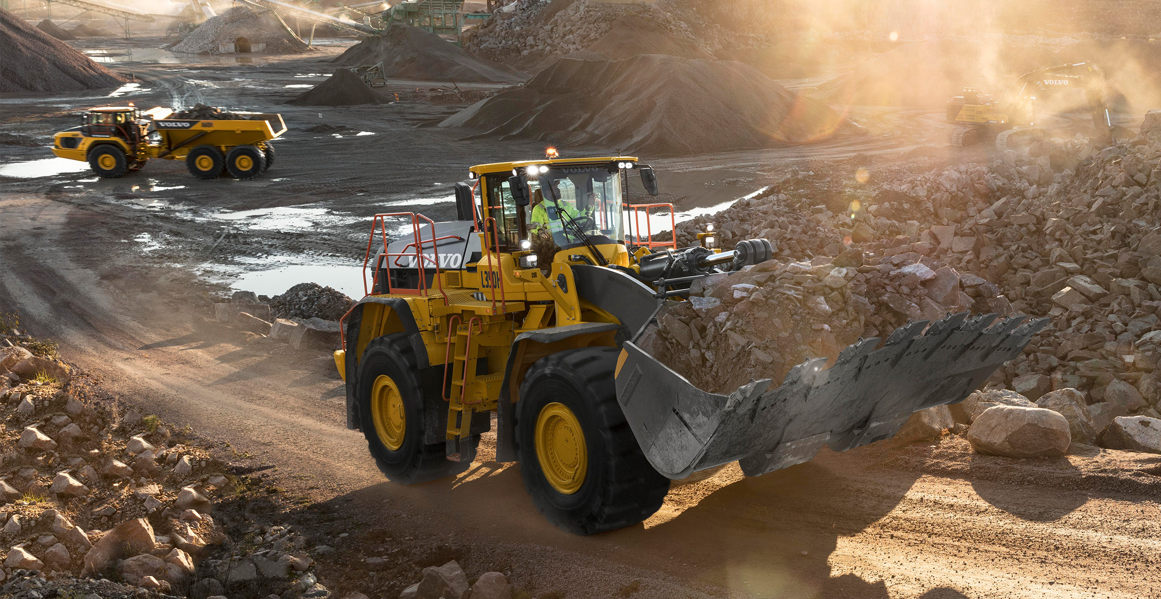 A Volvo wheel loader hauling rock through a quarry with a Volvo ADT in the background.