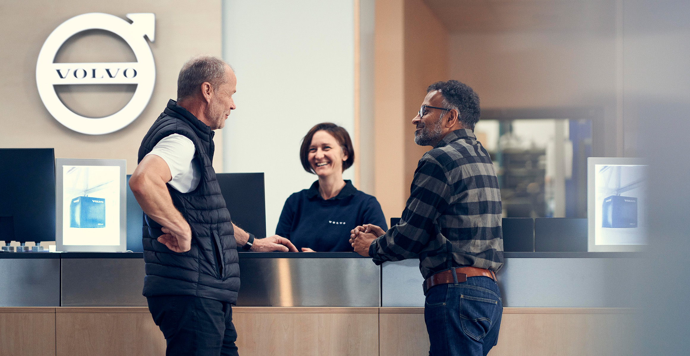 Two customers and a Volvo rep talking to each other at a Volvo Construction Equipment reception desk.
