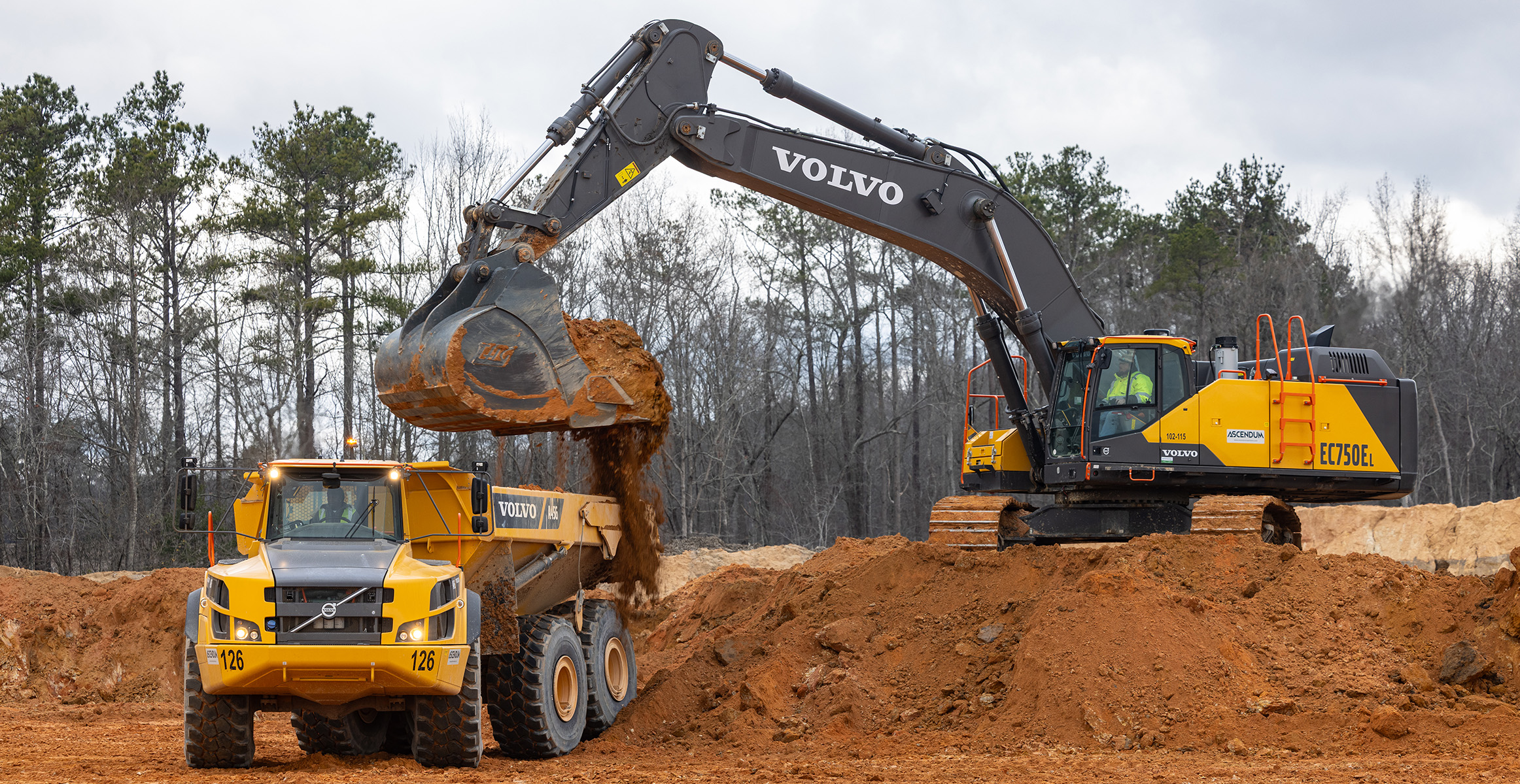 A Volvo EC750 excavator loading dirt into a Volvo articulated dump truck on a construction site.