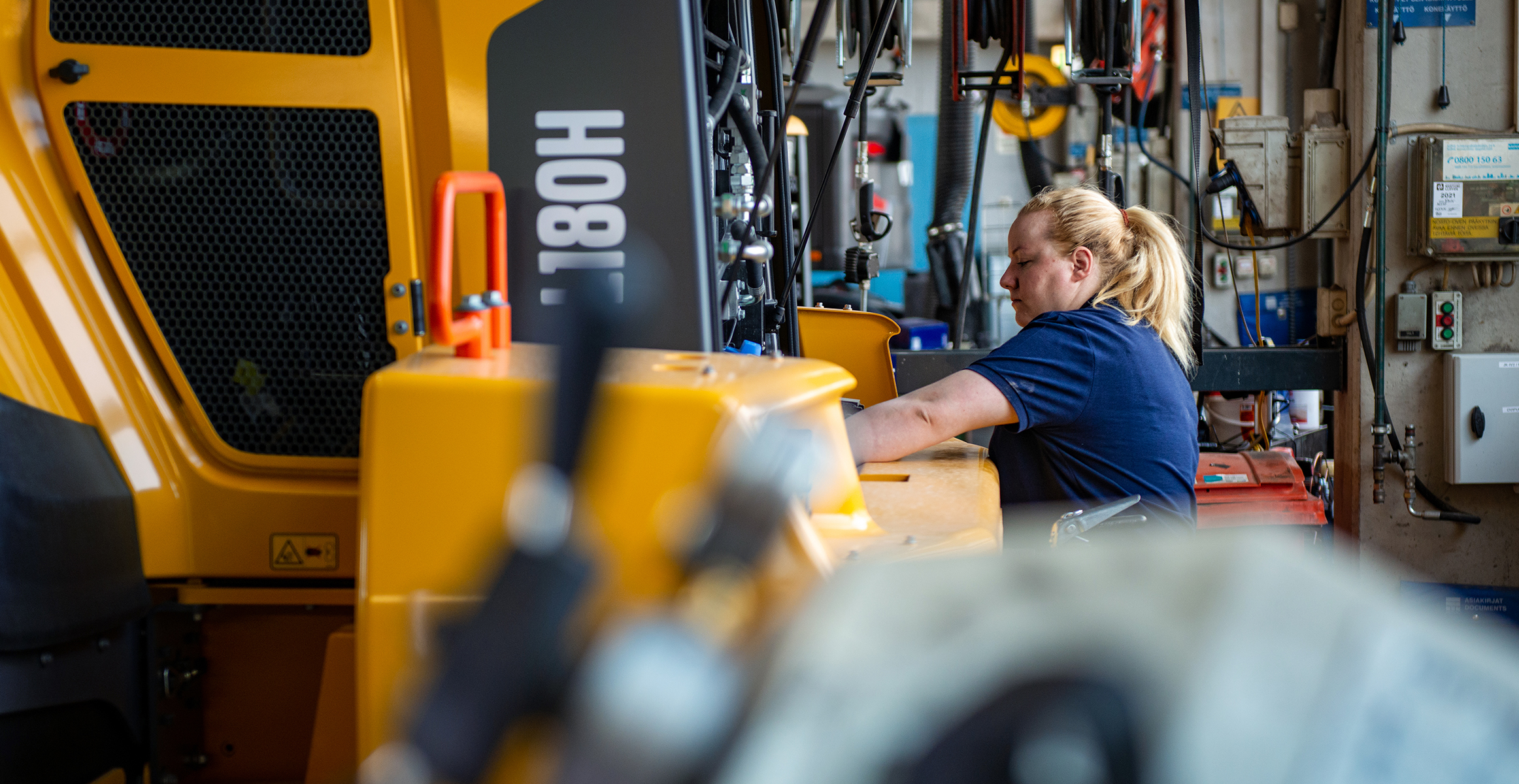 A heavy equipment technician servicing a Volvo L180H wheel loader in a service bay.