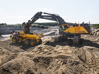 A Volvo EC750E excavator loading a Volvo A40 articulated dump truck in a quarry.