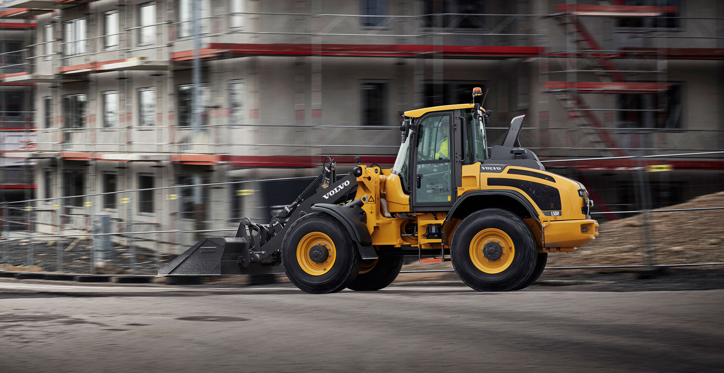 A Volvo wheel loader driving down a city street with the background blurred.