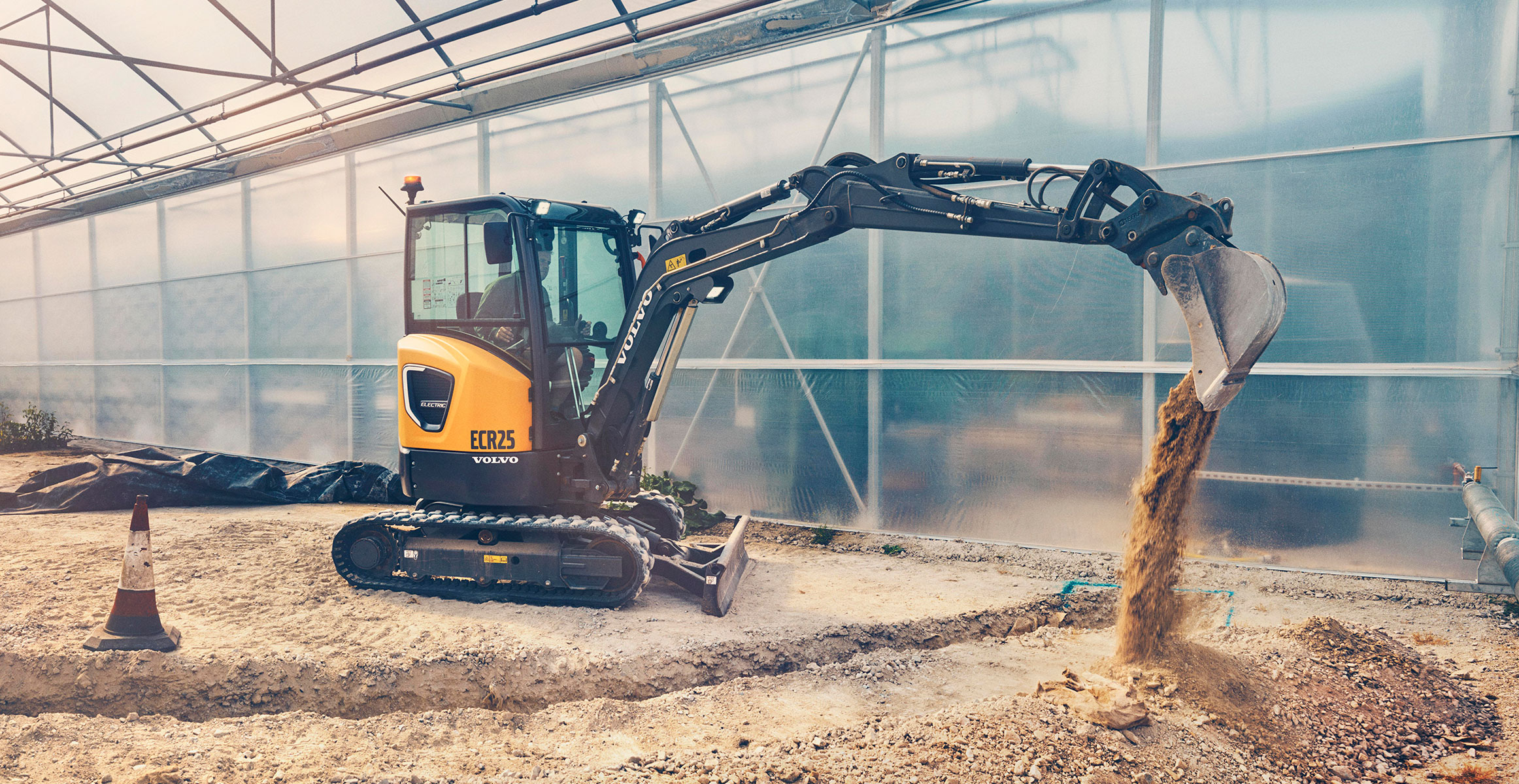 A Volvo ECR25 Electric excavator moving dirt in a greenhouse.