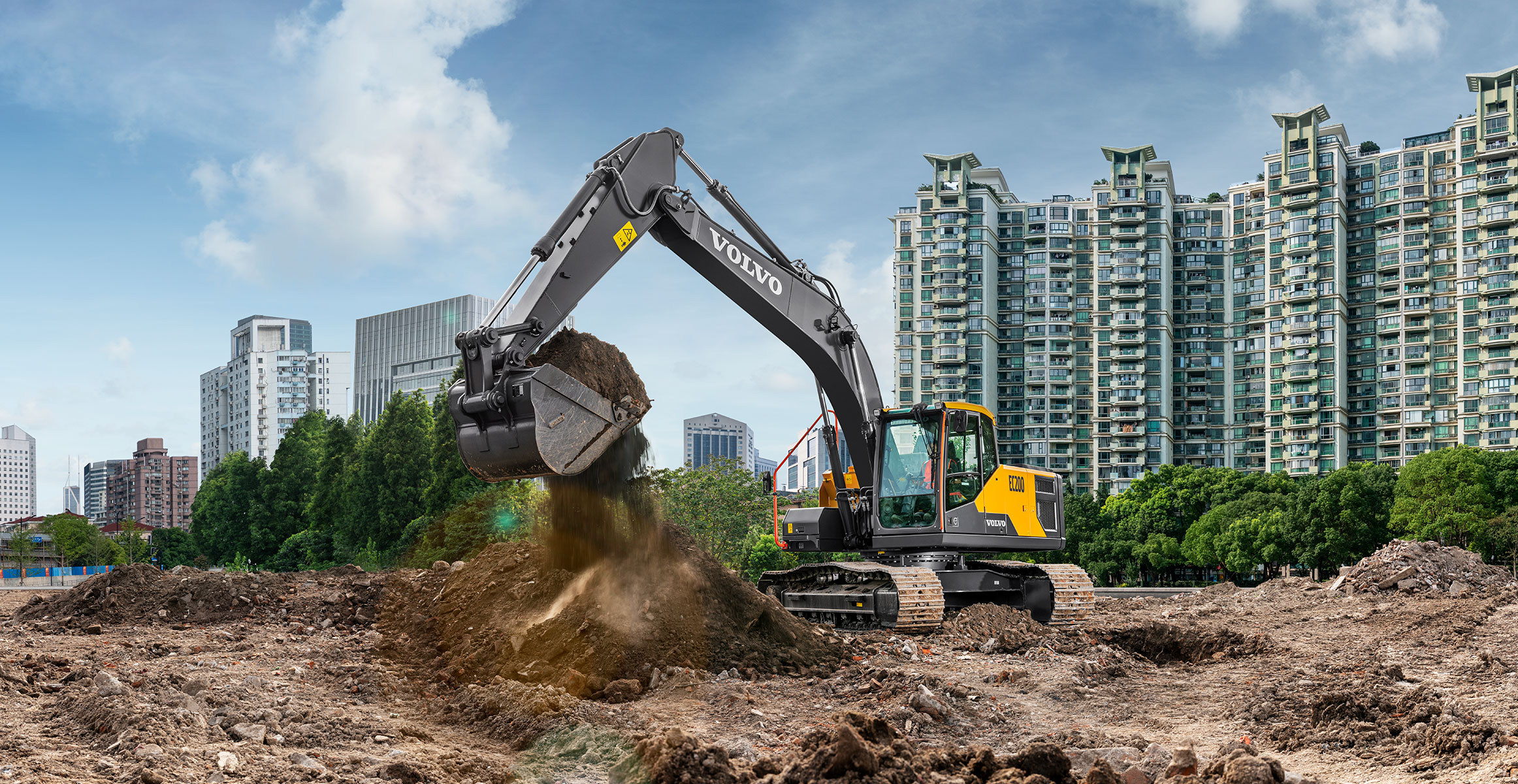 A Volvo excavator working in construction with a big city’s skyline in the background.
