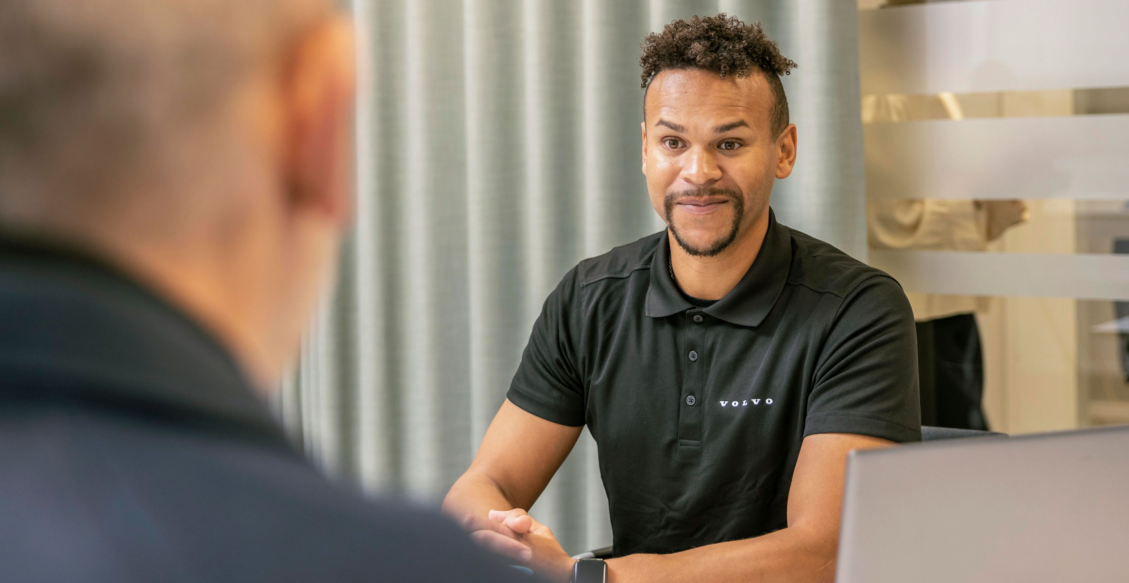 A customer having a conversation with a Volvo Financial Services rep at a desk.