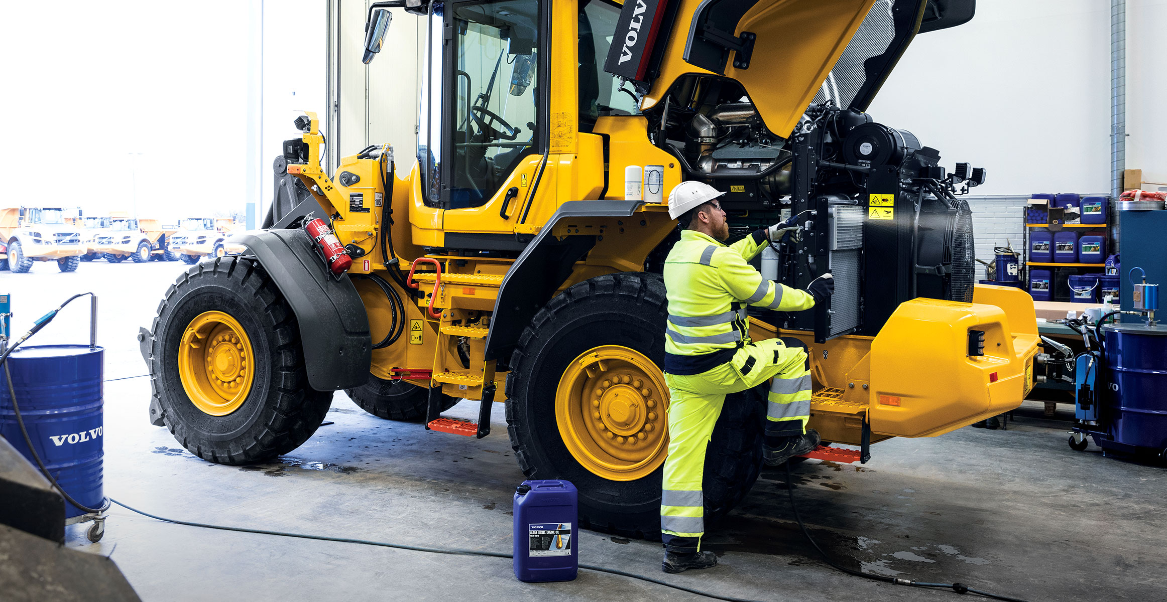 A technician servicing a Volvo wheel loader with the hood open.