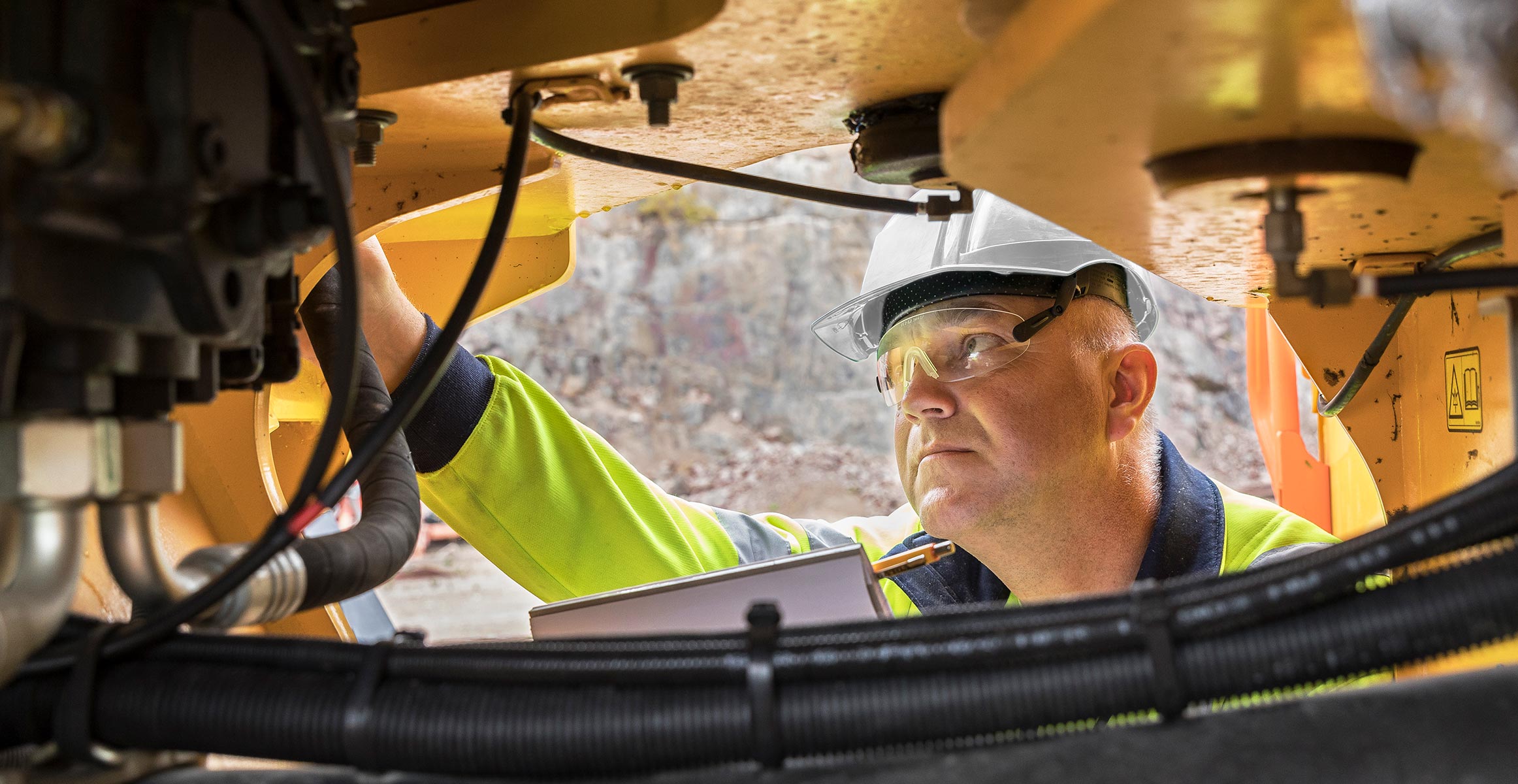 A service tech working under a piece of heavy construction equipment.