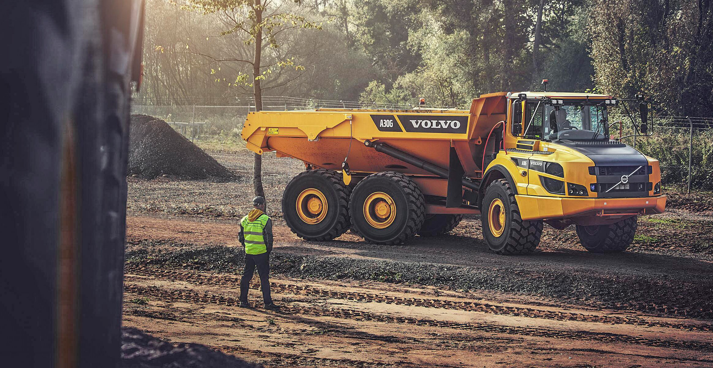 A construction worker standing and looking at a Volvo A30G articulated dump truck on a construction site.