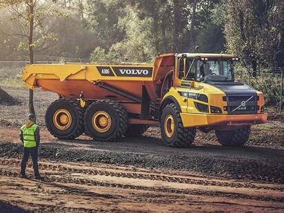A construction worker standing and looking at a Volvo A30G articulated dump truck on a construction site.