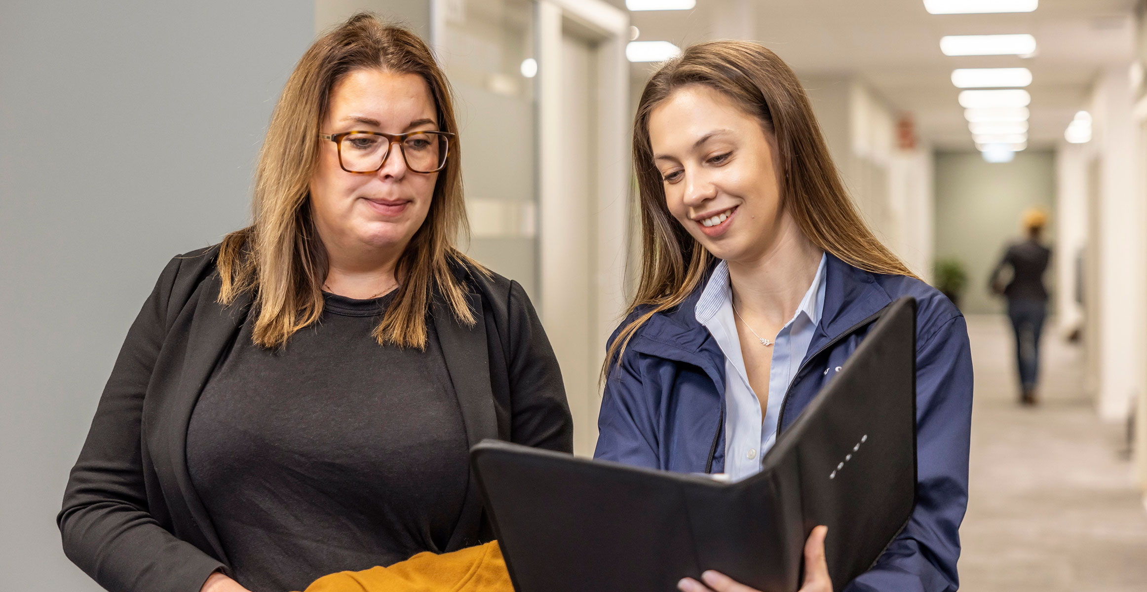 Two women at an office building walking down a hall and talking about construction equipment financing. 