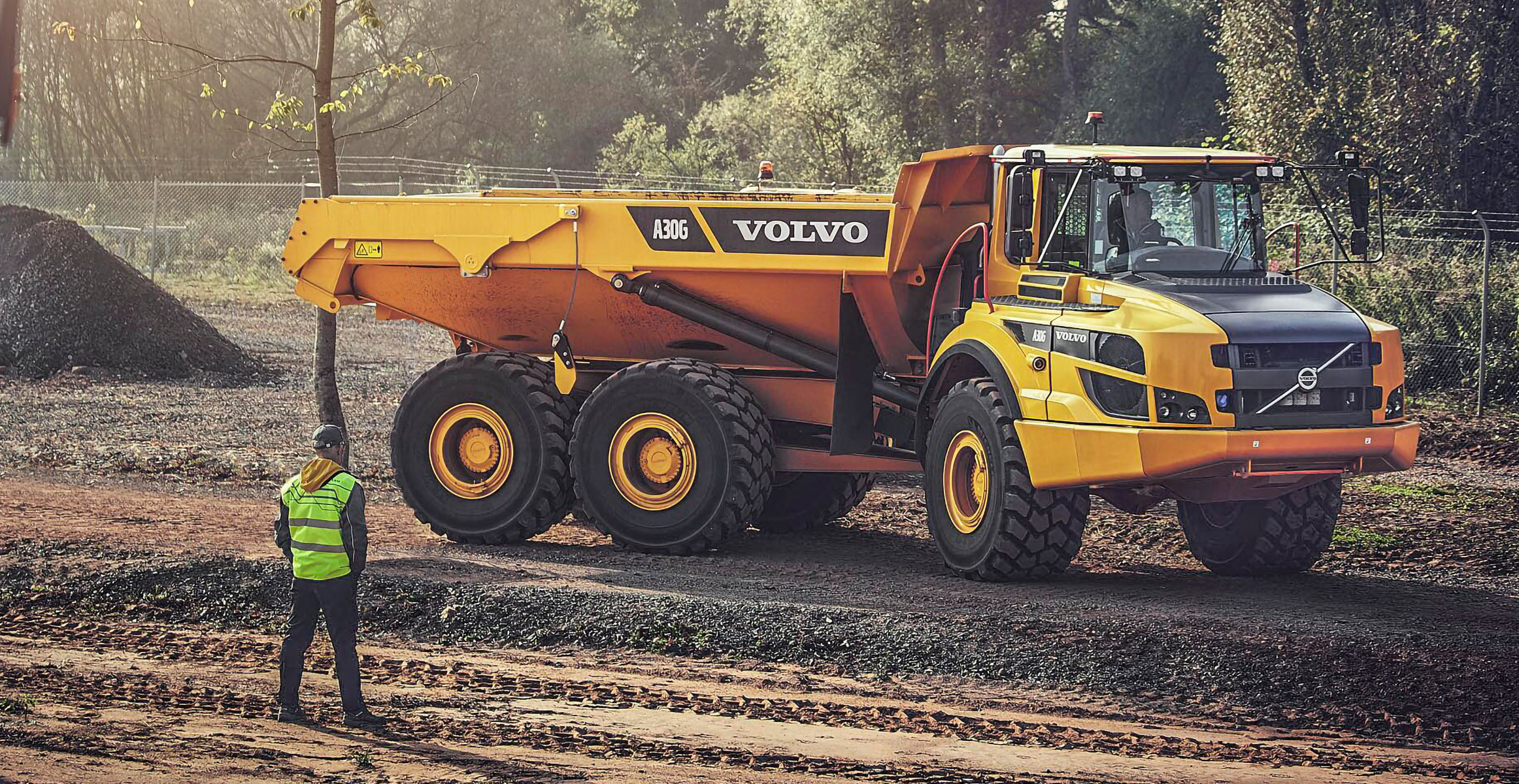 A Volvo A30G articulated dump truck working on a construction jobsite with another worker watching. 