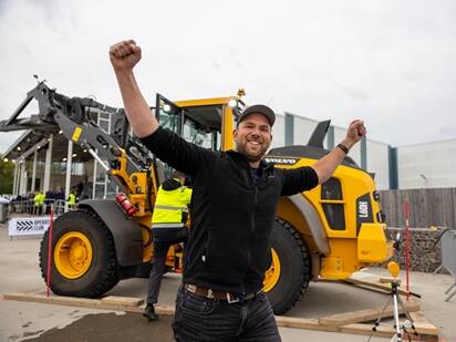 A contestant at the Volvo Operators Club Final celebrates after completing a challenge in front of a Volvo wheel loader.