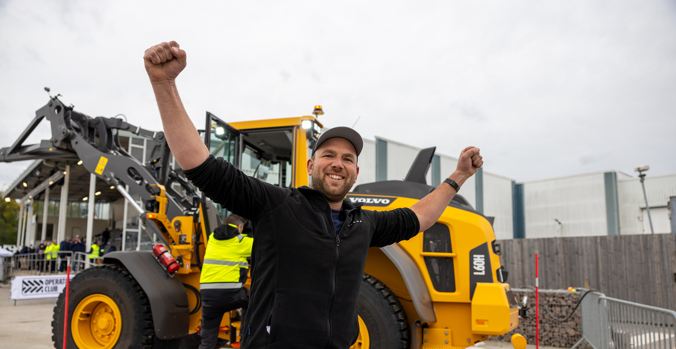 A contestant at the Volvo Operators Club Final celebrates after completing a challenge in front of a Volvo wheel loader.